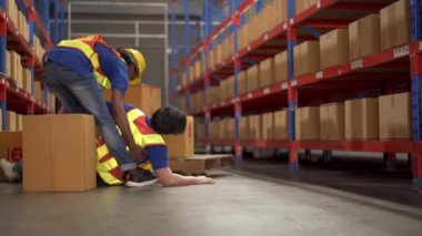 Dikkatsiz Asyalı bir depo çalışanı ağır bir karton kutuyu rafa kaldırıyor sonra kutunun bir kısmı düşüp kazara çarpıyor ve arkadaşı güvenli bir yere koşuyor ya da ona yardım ediyor. Çalışma alanında güvenlik talimatı.
