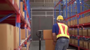 Dikkatsiz Asyalı bir depo çalışanı ağır bir karton kutuyu rafa kaldırıyor sonra kutunun bir kısmı düşüp kazara çarpıyor ve arkadaşı güvenli bir yere koşuyor ya da ona yardım ediyor. Çalışma alanında güvenlik talimatı.