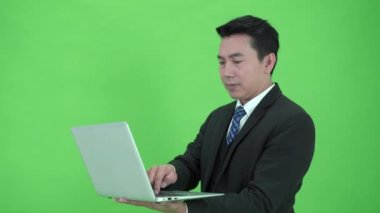Krom yeşil ekranda duran zeki ve yakışıklı Asyalı iş adamı dizüstü bilgisayar kullanıyor. Yeşil ekranda dizüstü bilgisayar tutan bir iş adamı..