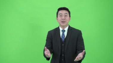 Krom yeşil ekranda duran zeki ve yakışıklı Asyalı iş adamı gülümsüyor ve el çırpıyor.