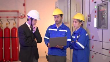 Asyalı elektrik mühendisi ekibinin portresi bir merkezi kontrol odasını inceliyor veya kontrol ediyor. Bakım odasında çalışan elektrik bakım mühendisleri..