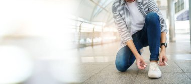 Asyalı genç adam yerde oturuyor ve kopyasıyla ayakkabı bağını bağlıyor. Şehirde ya da şehirde gezen ve ayakkabı bağı bağlayan bir adam.