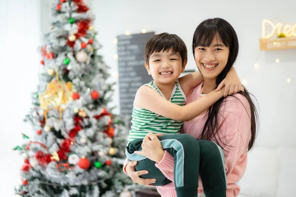 Happy cheerful Asian family, mother and lovely little son staying together in a bedroom that decorated in Christmas theme. Happy little boy playing with his mother or sister.