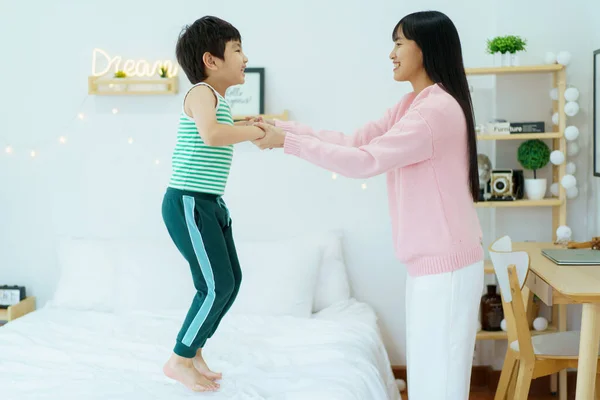 Happy cheerful Asian family, mother and lovely little son staying together in a bedroom that decorated in Christmas theme. Happy little boy playing with his mother or sister.