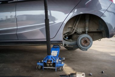 Hidrolik kriko kullanan teknisyen ya da tamirci arka tekerleği değiştirmek için arabayı kaldırır..