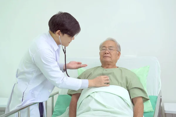 Elder Asian man sitting on the bed and talking to doctor about his physical injuries at his knees, elderly Asian man having a consulting with professional physical therapist or orthopedic doctor.