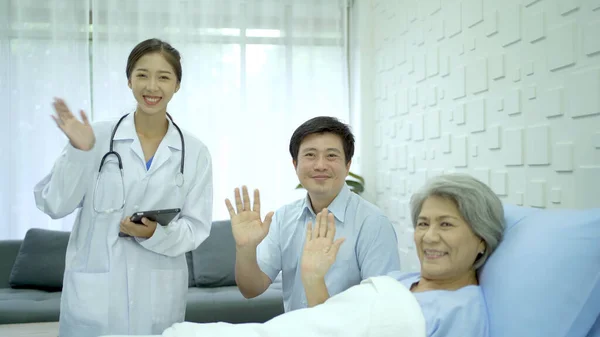 Happy specialist doctors and senior elder woman patient waving a hands to camera in recovery ward in hospital. Cheerful medical staffs and patient waving a hands to camera.