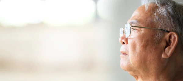Close up on senior Asian elder man living lonely and looking outside the window.