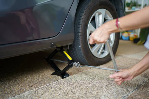 Unrecognizable woman using a car jack lifting up a car at rear wheel to change a broken or flat tyre. Female car driver using an emergency car jack lift up a car.