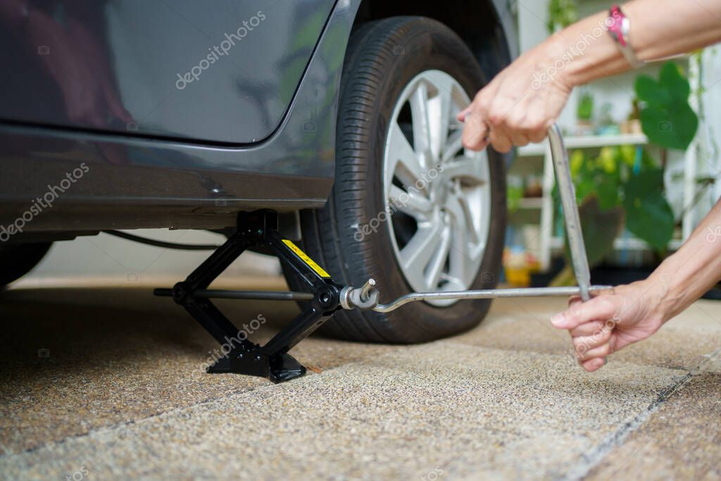 Mujer irreconocible usando un gato de coche levantando un coche en la