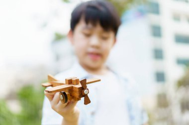 Asyalı küçük çocuk gelecekte pilot olmayı hayal eden tahta bir uçak oyuncağıyla oynuyor. Küçük çocukların pilotu olma hayali..