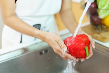 Yemek pişirmeden önce sağlıklı bir Asyalı kadın mutfak musluğunda sebze yıkıyor. Bir ev hanımı sağlıklı bir yemek pişirmek için meyve ve sebzeleri dikkatlice hazırlar ve temizler..