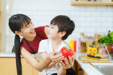 Mutlu anne ve küçük oğlu evcil mutfakta birlikte sebze ve yiyecek hazırlıyorlar. Anne ve oğlu mutfaktaki kameraya bakıp gülümsüyor..