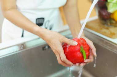 Yemek pişirmeden önce sağlıklı bir Asyalı kadın mutfak musluğunda sebze yıkıyor. Bir ev hanımı sağlıklı bir yemek pişirmek için meyve ve sebzeleri dikkatlice hazırlar ve temizler..