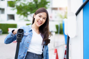 Tanımlanamayan Asyalı kadın, EV şarj istasyonunda CCS 2 EV konnektörünü tutuyor, bir EV-elektrikli araç hazırlıyor, bir aracı şarj etmek için..