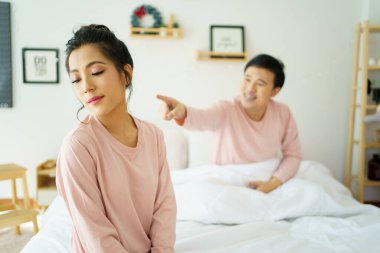 Mutsuz, stresli Asyalı bir adam karısı ona bağırırken yatakta oturuyor. Karı koca arasında ailevi bir sorun hakkında ciddi ya da kritik tartışmalar..