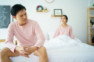 Mutsuz, stresli Asyalı bir adam karısı ona bağırırken yatakta oturuyor. Karı koca arasında ailevi bir sorun hakkında ciddi ya da kritik tartışmalar..