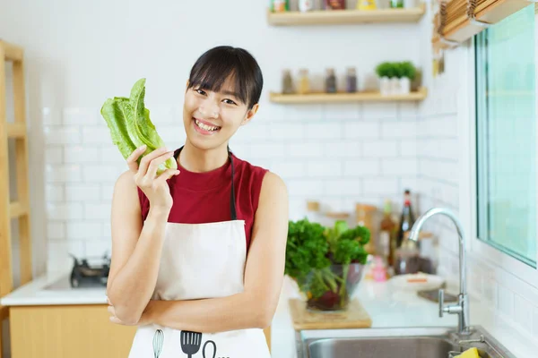 Happy healthy Asian woman washing a vegetables in domestic kitchen faucet before cooking. Cheerful healthy Asian woman carries a basket of vegetables and fruit and smiles to camera.