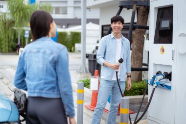 AC tip 2 EV 'yi tutan Asyalı erkek ve kadın EV şarj istasyonunda şarj oluyor. Yol aracı temiz enerji kavramına sahip seyahat veya ulaşım.