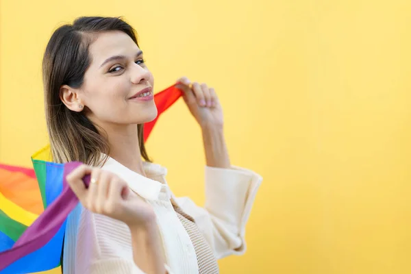 stock image Happy cheerful caucasian white woman smiling and holding a rainbow flag which is the symbolic of LGBTQ people on yellow background. The diversity in genders and lifestyles concept.