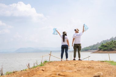 Bir grup Asyalı genç gönüllü parktaki plastik şişe çöplerini toplamaya ya da toplamaya yardım ediyor. Sürdürülebilirlik ve çevre koruma kavramı.