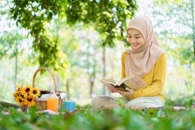 Mutlu, Asyalı, güzel Müslüman kadın parkta yerde oturuyor ve öğleden sonra bir fincan çay içiyor. Güzel Müslüman kadın hafta sonu dinleniyor ve piknik yapıyor..