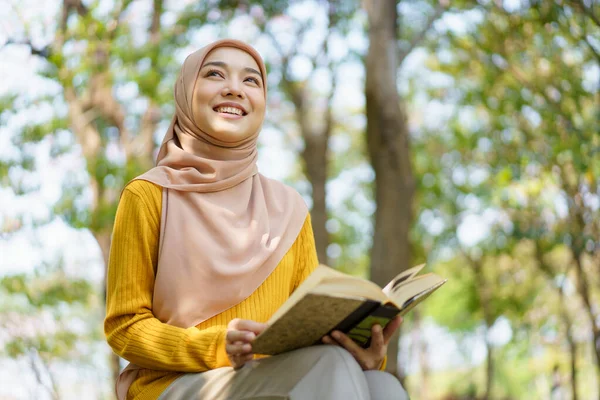 幸せな陽気なアジアの美しいイスラム教徒の女性の本を読んで コーランの木の下に イスラームを学ぶムスリム女子学生コーラン — ストック写真