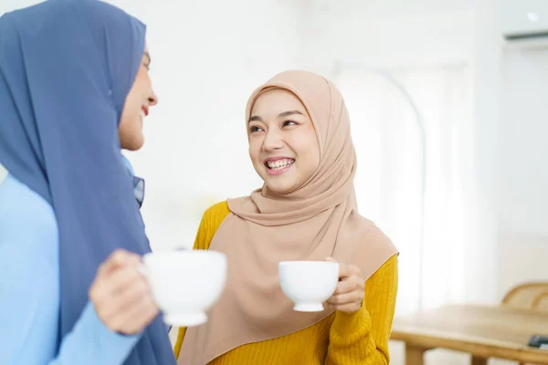 明るいアジア系ムスリム女性がリビングルームでお茶やコーヒーを飲みながらビジネスについて話し合います 現代のイスラム教徒のライフスタイルコンセプト — ストック写真