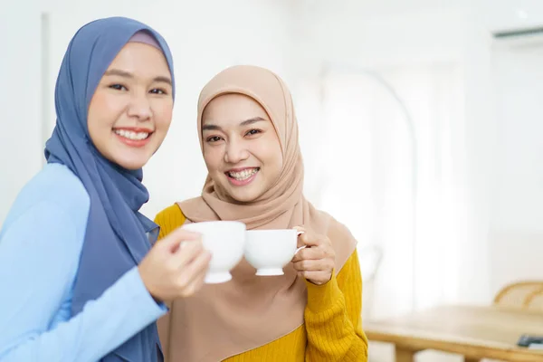 明るいアジア系ムスリム女性がリビングルームでお茶やコーヒーを飲みながらビジネスについて話し合います 現代のイスラム教徒のライフスタイルコンセプト — ストック写真