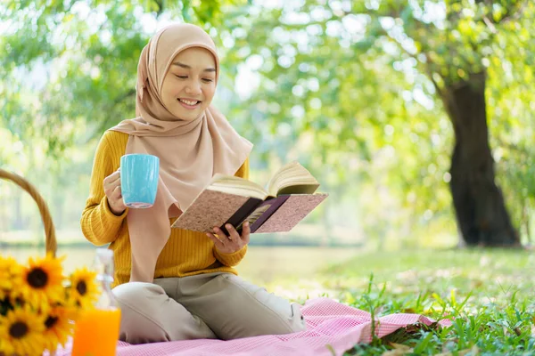 公園の地面に座って午後にお茶を飲んでいる幸せな陽気なアジアの美しいイスラム教徒の女性 美しいイスラム教徒の女性は週末にリラックスしてピクニック — ストック写真