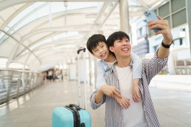 Mutlu Asyalı adam ve küçük çocuk tren istasyonunda seyahat ediyor ve fotoğraf çekmek için akıllı telefonu kullanıyor. Baba ve oğul fotoğraf çekmek için akıllı telefon kullanıyor..