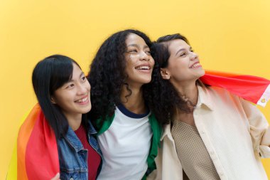 Mutlu mutlu LGBTQ çok ırklı kadınlar fotoğraf için poz veriyor ve sarı arka planda gökkuşağı bayrağı var. LGBTQ insanlarının ifade özgürlüğü.