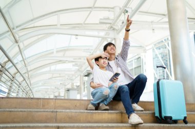 Mutlu Asyalı aile şehir merkezinde birlikte seyahat ediyor. Baba, oğluyla birlikte tren istasyonunun haritasına bakıyor ve baş parmağını gösteriyor..