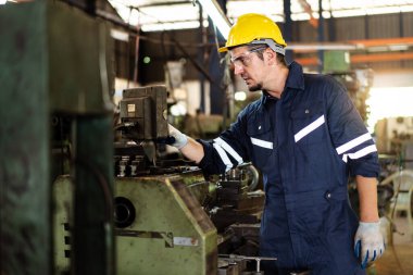 Beyaz ırktan profesyonel beyaz erkek teknisyen torna fabrikasında ağır iş makinesini çalıştırıyor. Güvenlik teknisyeni ve kask giysisi fabrikada bir makineyi kontrol ediyor..