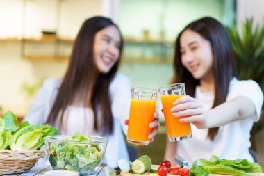 Asyalı kadınlar kahvaltı yapmayı ve yemek odasında organik portakal suyu içmeyi seviyorlar. Tatlı Asyalı kadınlar birlikte portakal suyunu yudumluyorlar..