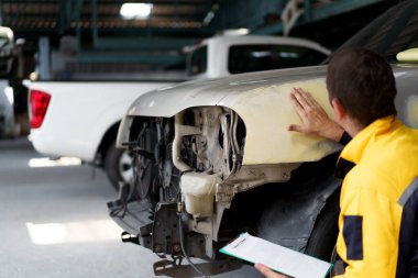 Uzman otomotiv teknisyeni garajdaki hasarlı aracı inceliyor. Araba makine mühendisi ya da teknisyeni tamir etmeden önce arabayı kontrol edip kontrol ediyor..