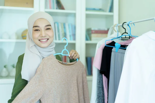 快乐快乐的亚洲年轻的穆斯林女人在衣架上选择更衣室里的衣服 穆斯林的现代生活方式概念 — 图库照片