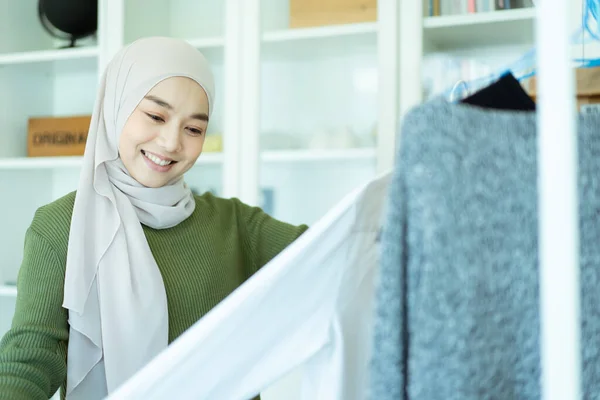 幸せな陽気なアジアの若いイスラム教徒の女性の服ハンガーにフィッティングルームで服を選択します 現代のイスラム教徒のライフスタイル概念 — ストック写真