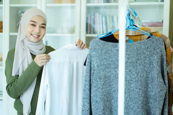 幸せな陽気なアジアの若いイスラム教徒の女性の服ハンガーにフィッティングルームで服を選択します 現代のイスラム教徒のライフスタイル概念 — ストック写真