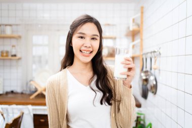Güzel mutlu Asyalı kadın sabah mutfakta süt içiyor ve kameraya gülümsüyor. Mutlu Asyalı kadın bir bardak süt ve gülümseme gösteriyor..