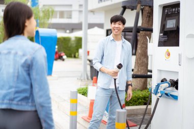 AC tip 2 EV 'yi tutan Asyalı erkek ve kadın EV şarj istasyonunda şarj oluyor. Yol aracı temiz enerji kavramına sahip seyahat veya ulaşım.