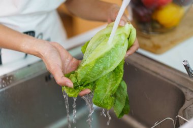 Yemek pişirmeden önce sağlıklı bir Asyalı kadın mutfak musluğunda sebze yıkıyor. Bir ev hanımı sağlıklı bir yemek pişirmek için meyve ve sebzeleri dikkatlice hazırlar ve temizler..
