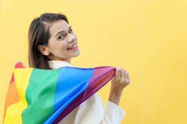 Mutlu beyaz kadın gülümsüyor ve elinde sarı arka planda LGBTQ insanlarının sembolü olan gökkuşağı bayrağı taşıyor. Cinsiyet ve yaşam tarzlarındaki çeşitlilik.