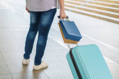 Asyalı genç bir adam valizini şehir boyunca ya da havaalanı terminali boyunca alışveriş torbalarıyla sürüklüyor. Şehirde ya da şehir merkezinde seyahat eden bir adam.