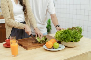 Mutlu Asyalı çift mutfakta organik sebze salatası yapıyor. Yemek bıçağı kullanan kadın sebze kesiyor. Sağlıklı yeme kavramı.