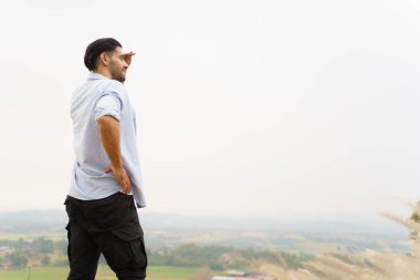 Mutlu yakışıklı Orta Doğu Asyalı adam dağda duruyor ve güzel manzara manzarası ile rahatlıyor. Adam dağın tepesine tırmanıp fotoğraf çekmek için poz veriyor..