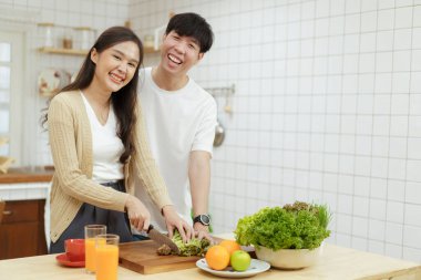 Mutlu Asyalı çift mutfakta organik sebze salatası yapıyor. Yemek bıçağı kullanan kadın sebze kesiyor. Sağlıklı yeme kavramı.