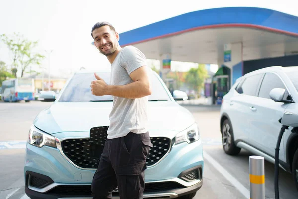 Yakışıklı Asyalı genç adam EV prizini tutuyor ve arabaya takıyor, EV bağlantısını takıyor..