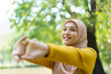 Mutlu mutlu Asyalı güzel bayan müslüman egzersiz yapıyor ve parka yakın bir yerde fotokopi aletiyle esniyor. Modern Müslüman kadın yaşam tarzları ve çeşitlilik kavramı.