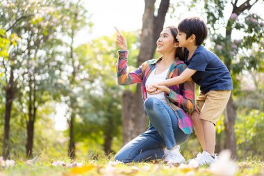 Asyalı bir kadın ve çocuk parkta güzel bir bokeh eşliğinde oynuyorlar ve arka plan kopyalama alanını aydınlatıyorlar. Küçük tatlı çocuk annesini arkadan öpüyor..